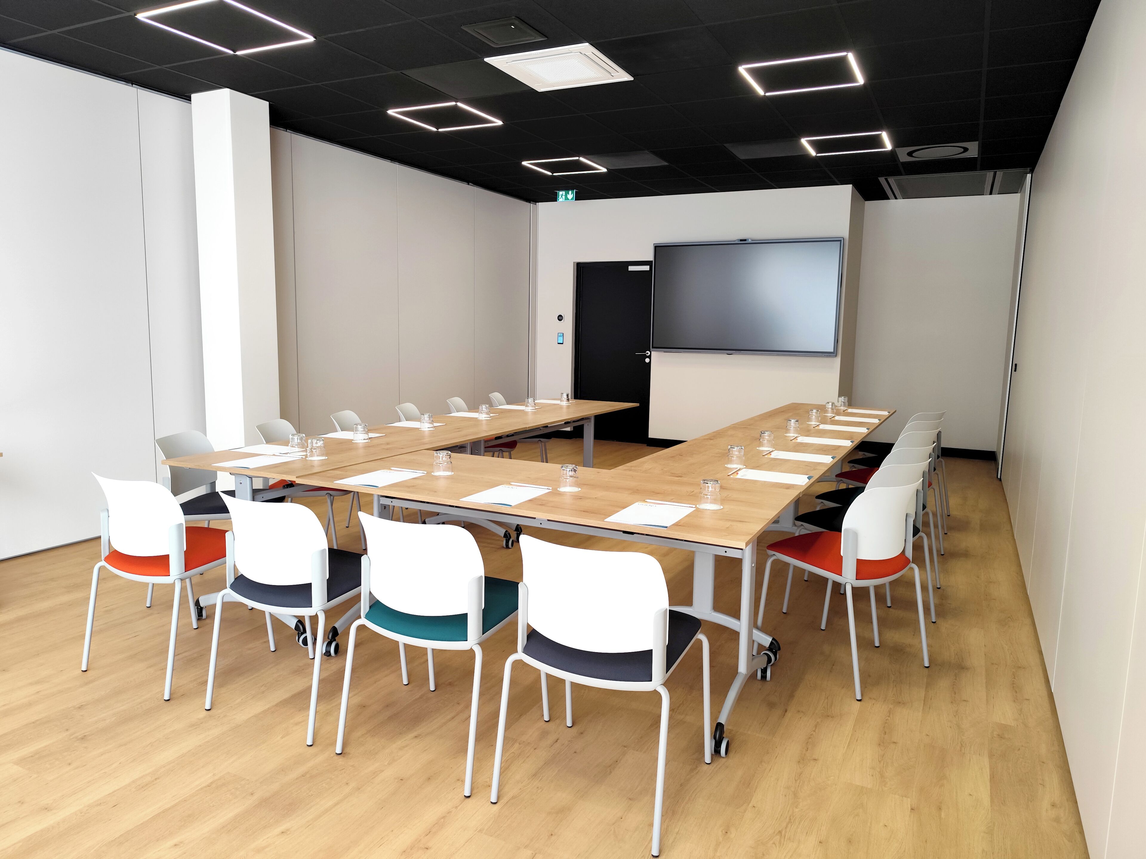 A conference room with a long table, white chairs, and a projector screen.