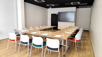 Uma sala de conferência com uma mesa comprida, cadeiras brancas e uma tela de projeção.