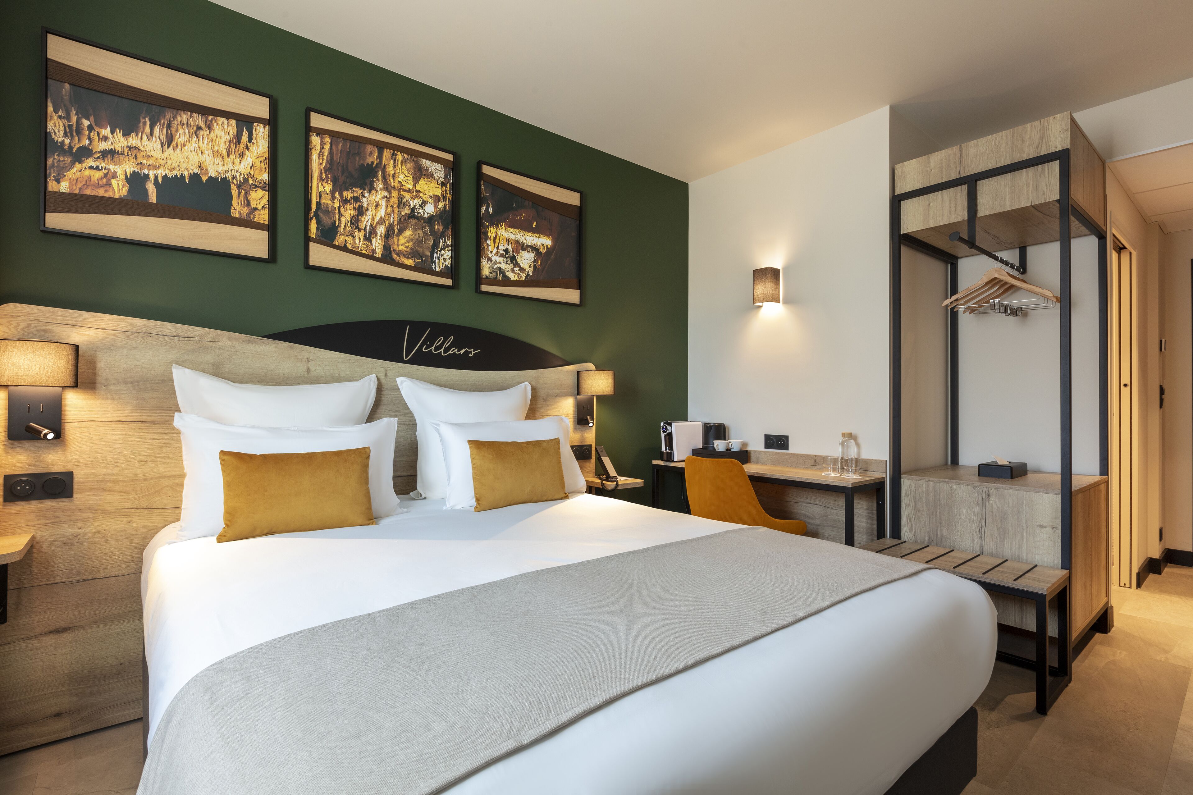 A hotel room with a large bed, a desk, and a seating area. There are three framed pictures on the wall and a sign above the bed that reads "Villa."