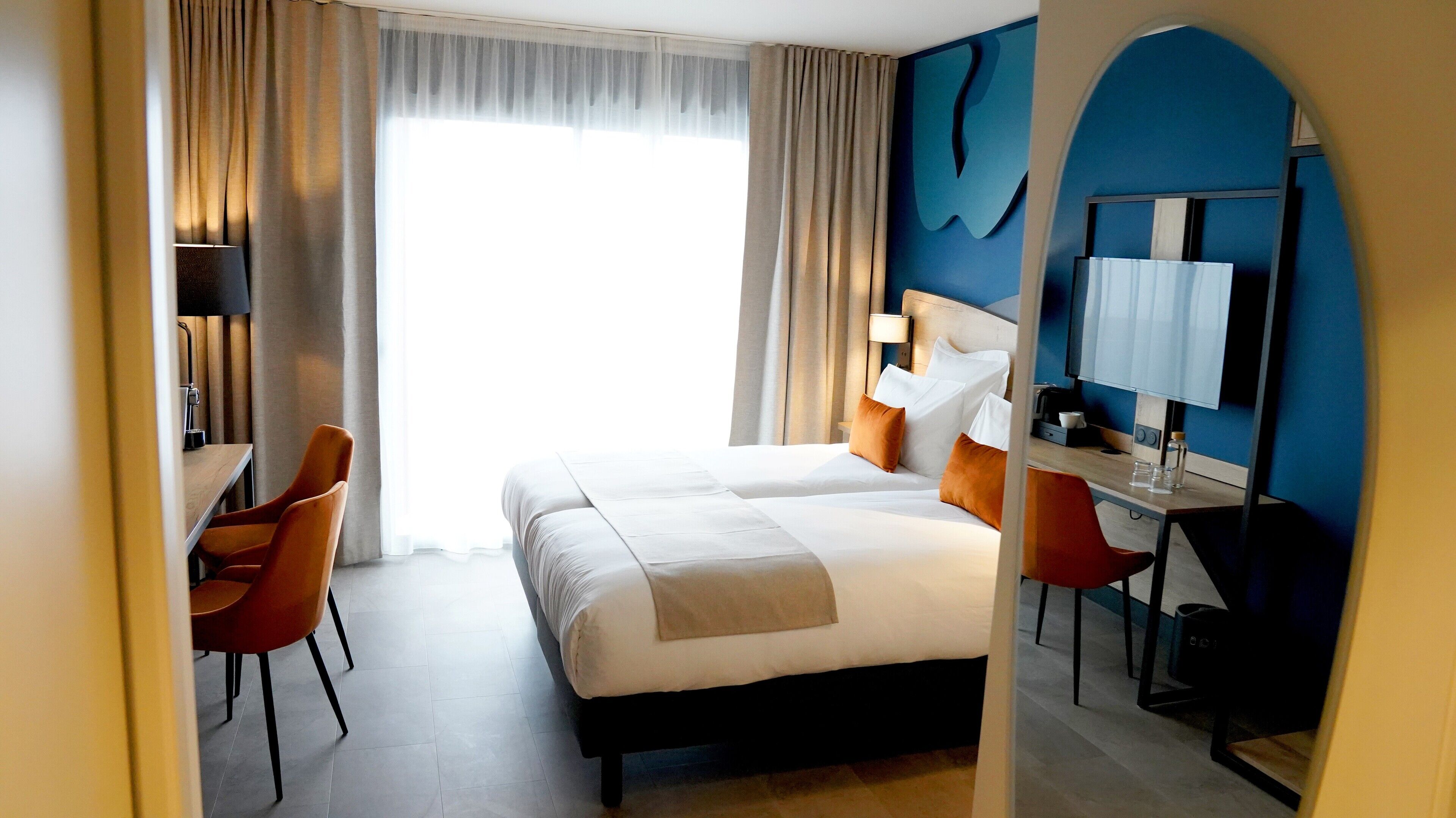 Una habitación de hotel con una cama, dos mesitas de noche, un escritorio y una silla.