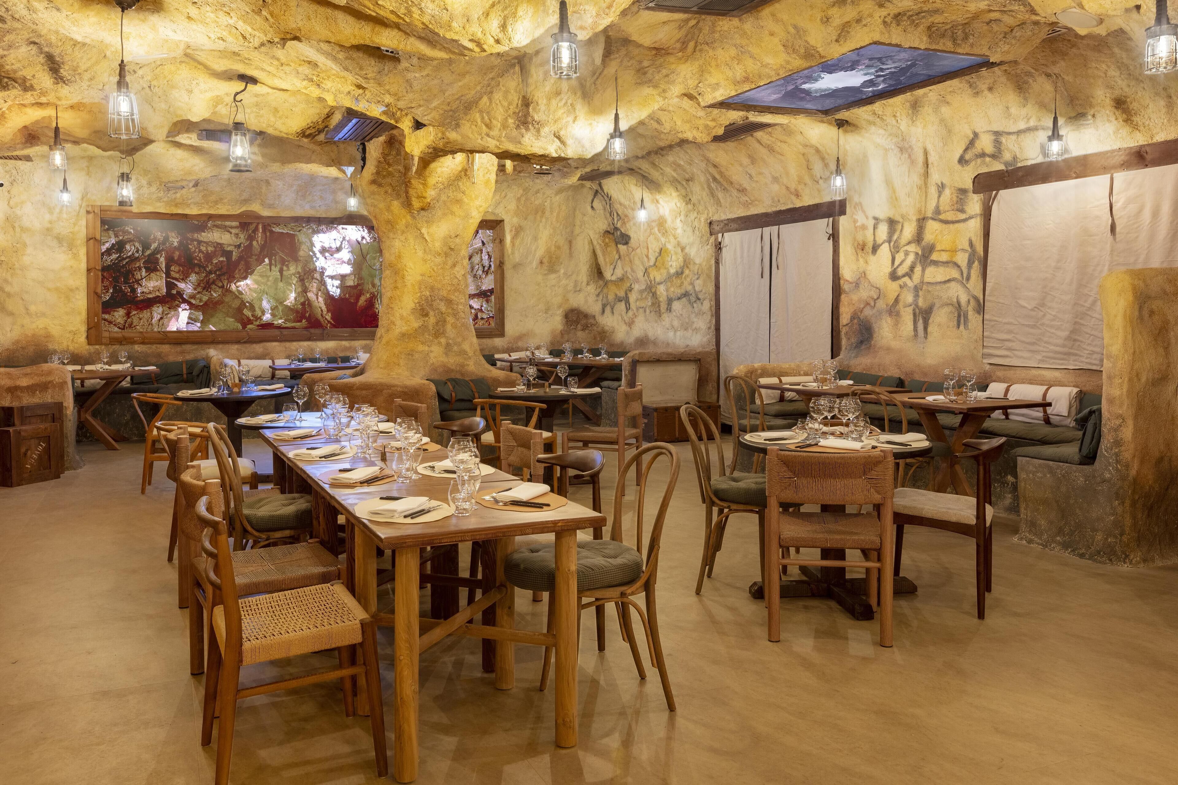 A restaurant with wooden tables and chairs, a large mural on the wall, and hanging light fixtures.
