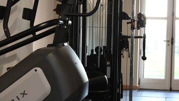 Un gimnasio en casa con una bicicleta estática, máquinas de pesas y una puerta que da a una habitación luminosa.