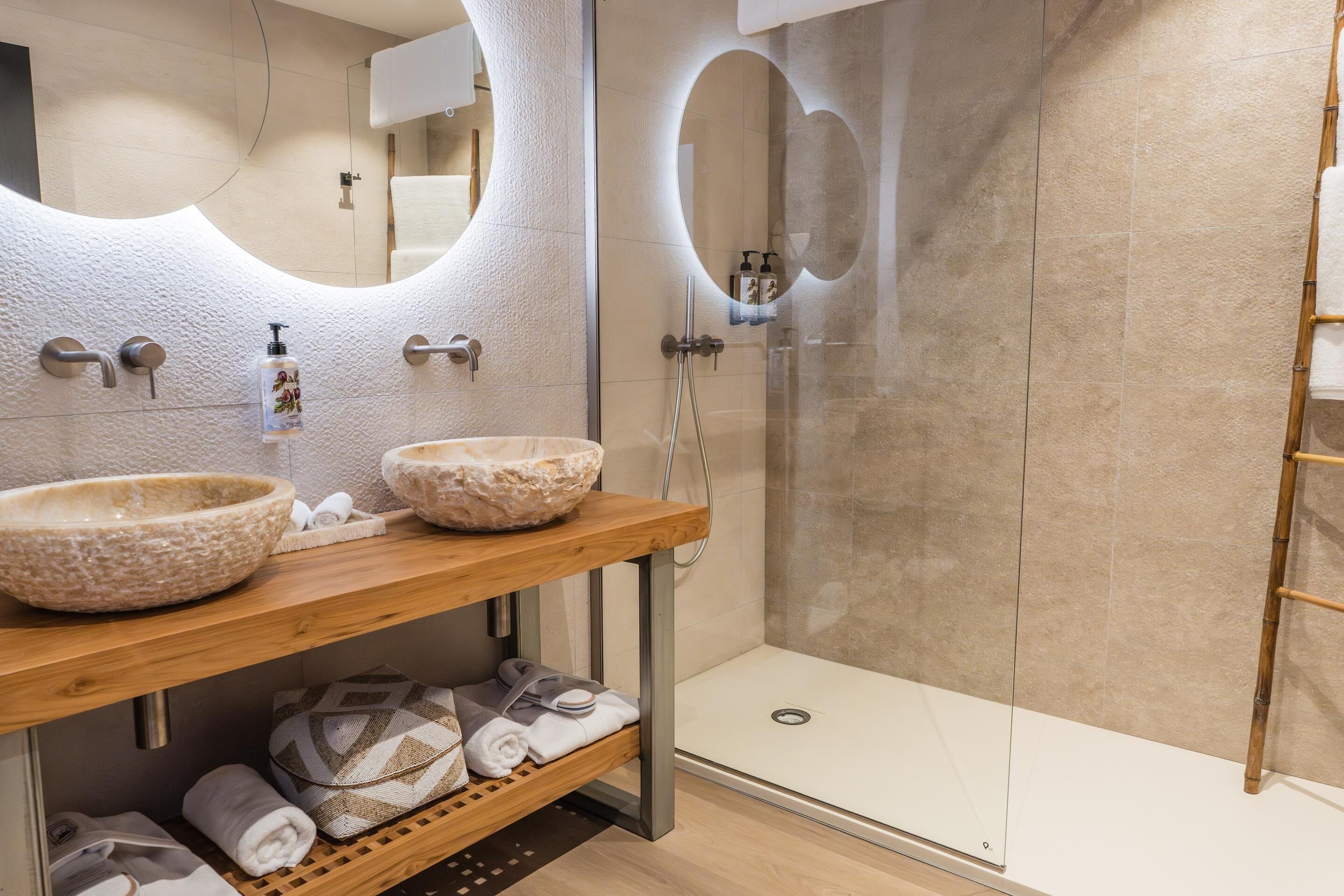 A modern bathroom with two large stone sinks, a wooden vanity, a glass shower enclosure, and neatly folded towels.