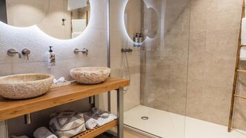 Une salle de bain moderne avec deux grands lavabos en pierre, un meuble-lavabo en bois, une cabine de douche en verre et des serviettes soigneusement pliées.