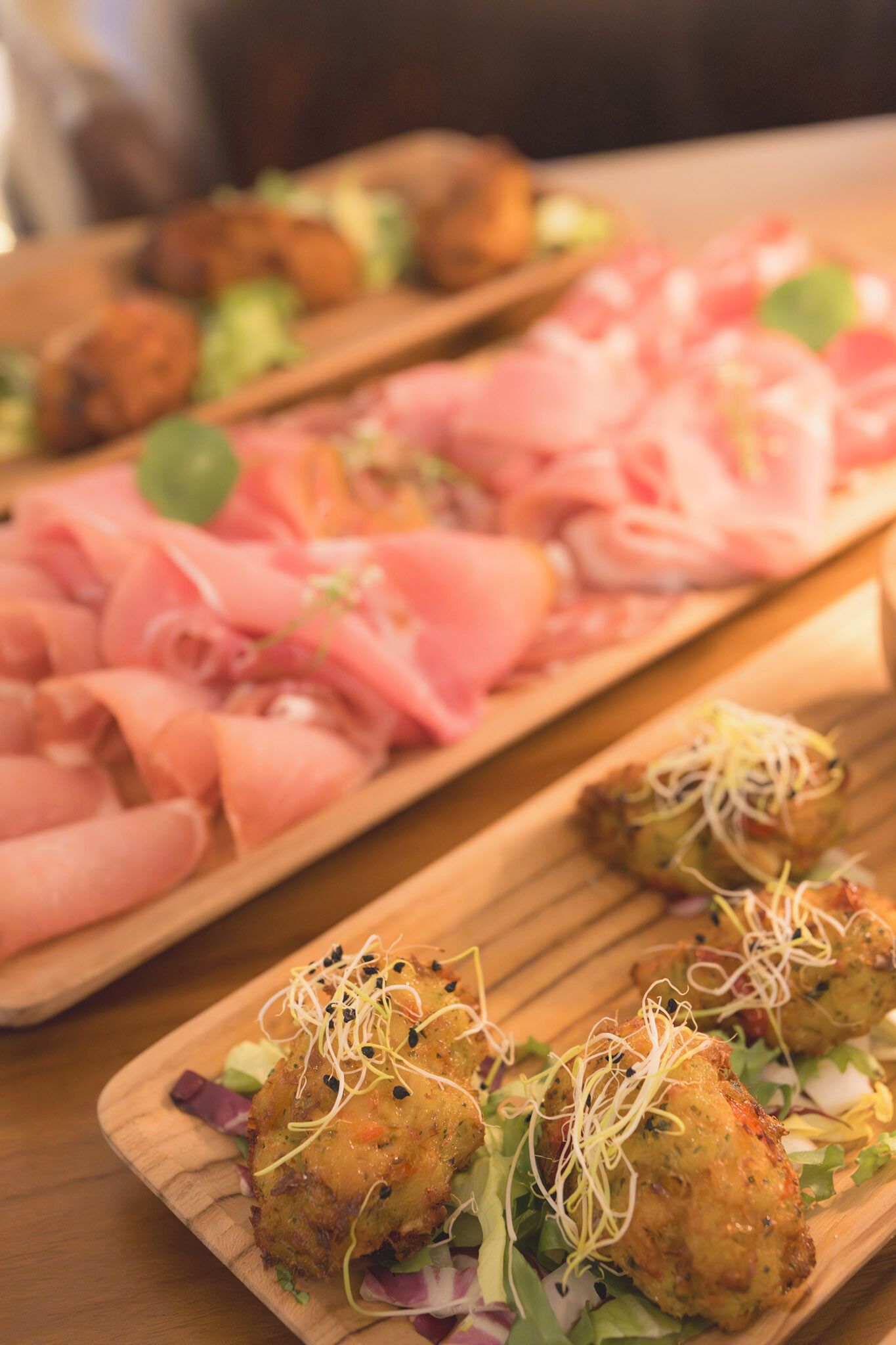 A wooden board with various food items, including what appears to be breaded and fried items, and sliced meats.