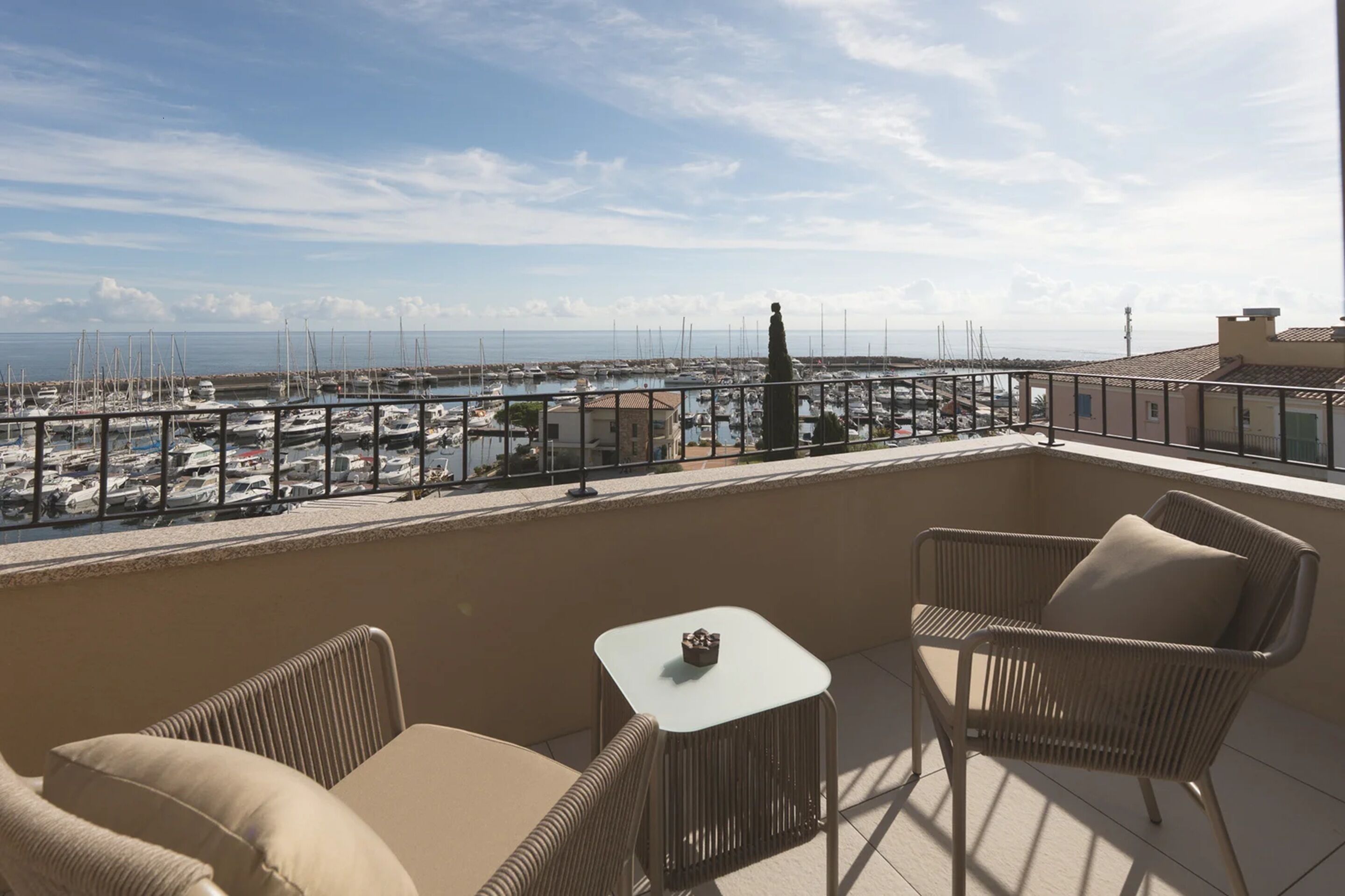 Een balkon met rieten meubels, een tafeltje en uitzicht op een jachthaven met boten.