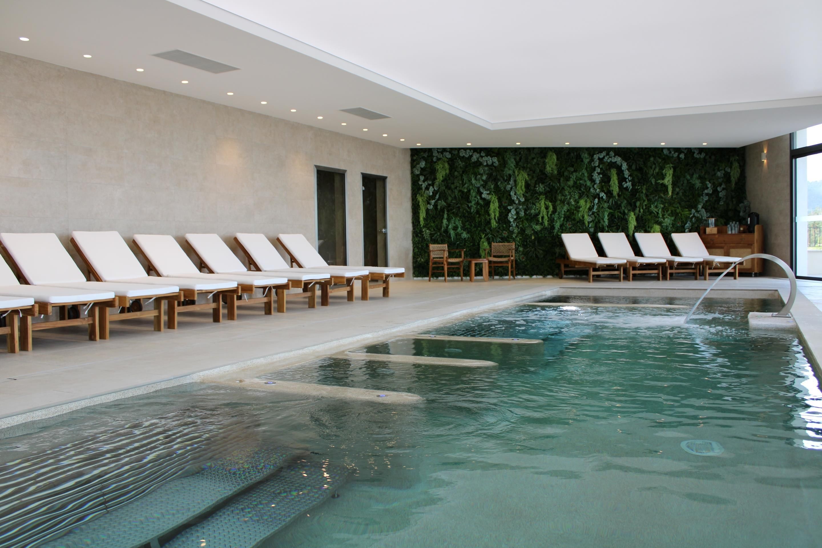 Un'area piscina interna moderna con poltrone relax e una parete verde.