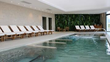 Un'area piscina interna moderna con poltrone relax e una parete verde.