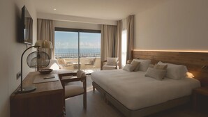 A hotel room with a large bed, a desk with a lamp, a chair, and a view of the sea through a large window. - Best Western Premier A Storia Solenzara (Sari-Solenzara)