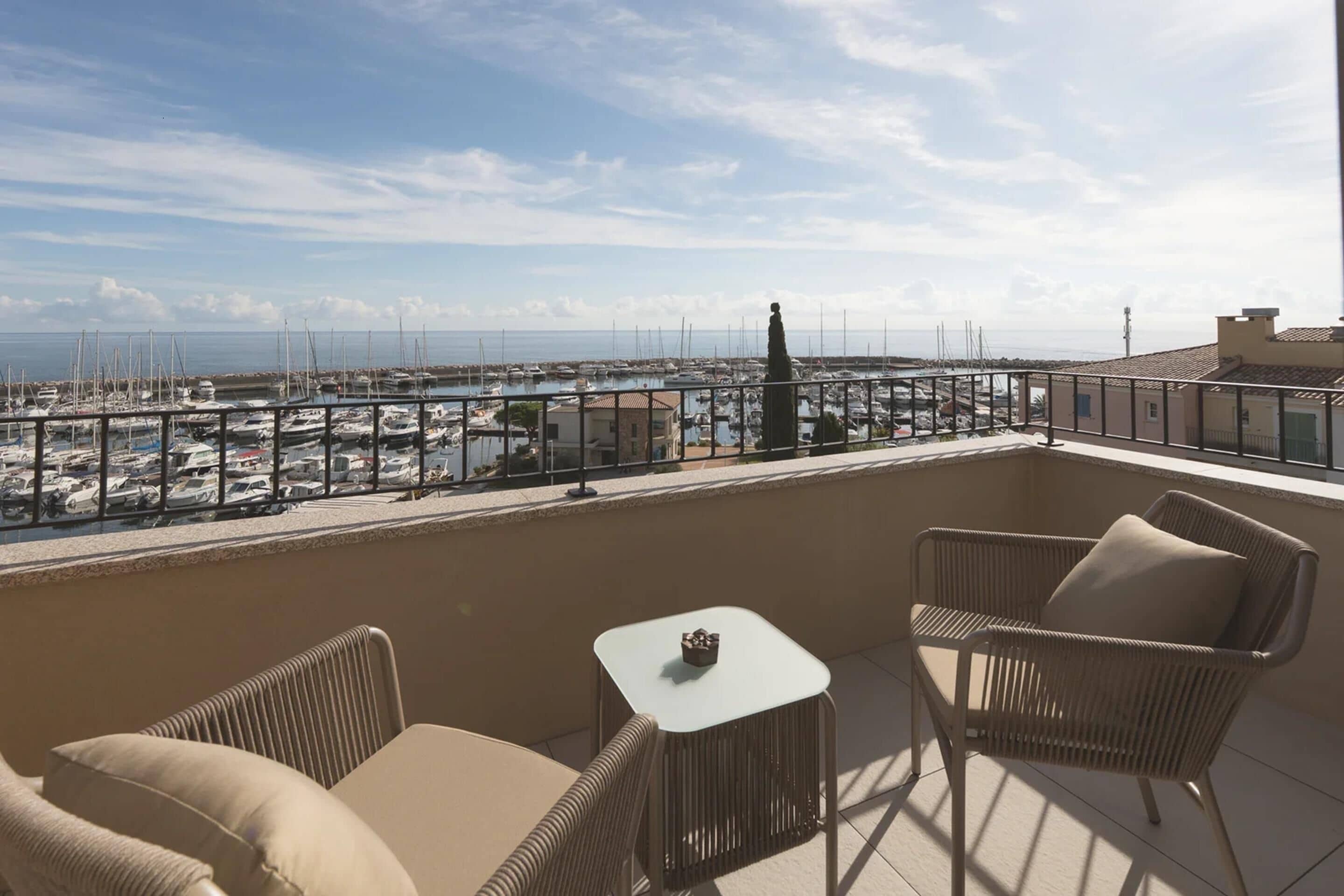 Un balcon doté de meubles en osier et offrant une vue sur un port de plaisance.