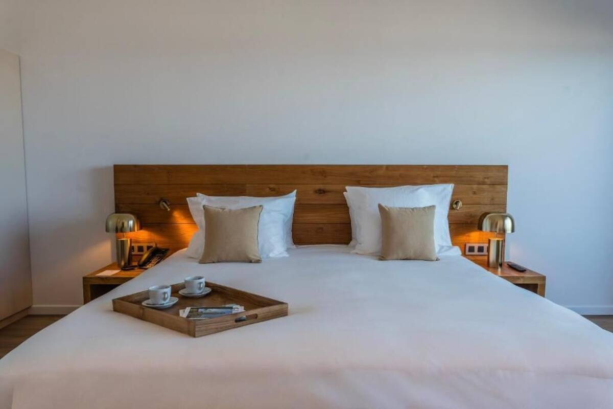 A neatly made bed with a wooden headboard, two bedside lamps, and a tray with cups and a book on the bed.