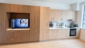 A modern kitchen with wooden cabinetry, a built-in oven, and a flat-screen TV mounted on the wall.