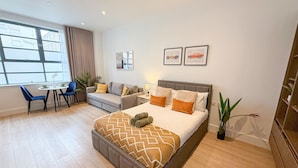 A modern hotel room with a large bed, a desk with a chair, a sofa, and a dining table.