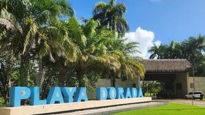 Schild für Playa Dorada, mit freiem Blick auf die umliegenden Palmen und ein Gebäude im Hintergrund.
