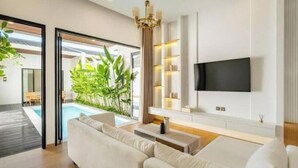 Una sala de estar moderna con un televisor grande, un sofá y vistas a una piscina y vegetación.