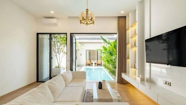 Una sala de estar moderna con un sofá grande, un televisor de pantalla plana y vista a una piscina.