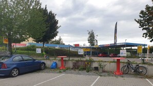 Uma área de estacionamento com um carro azul, mesas vermelhas e uma bicicleta.