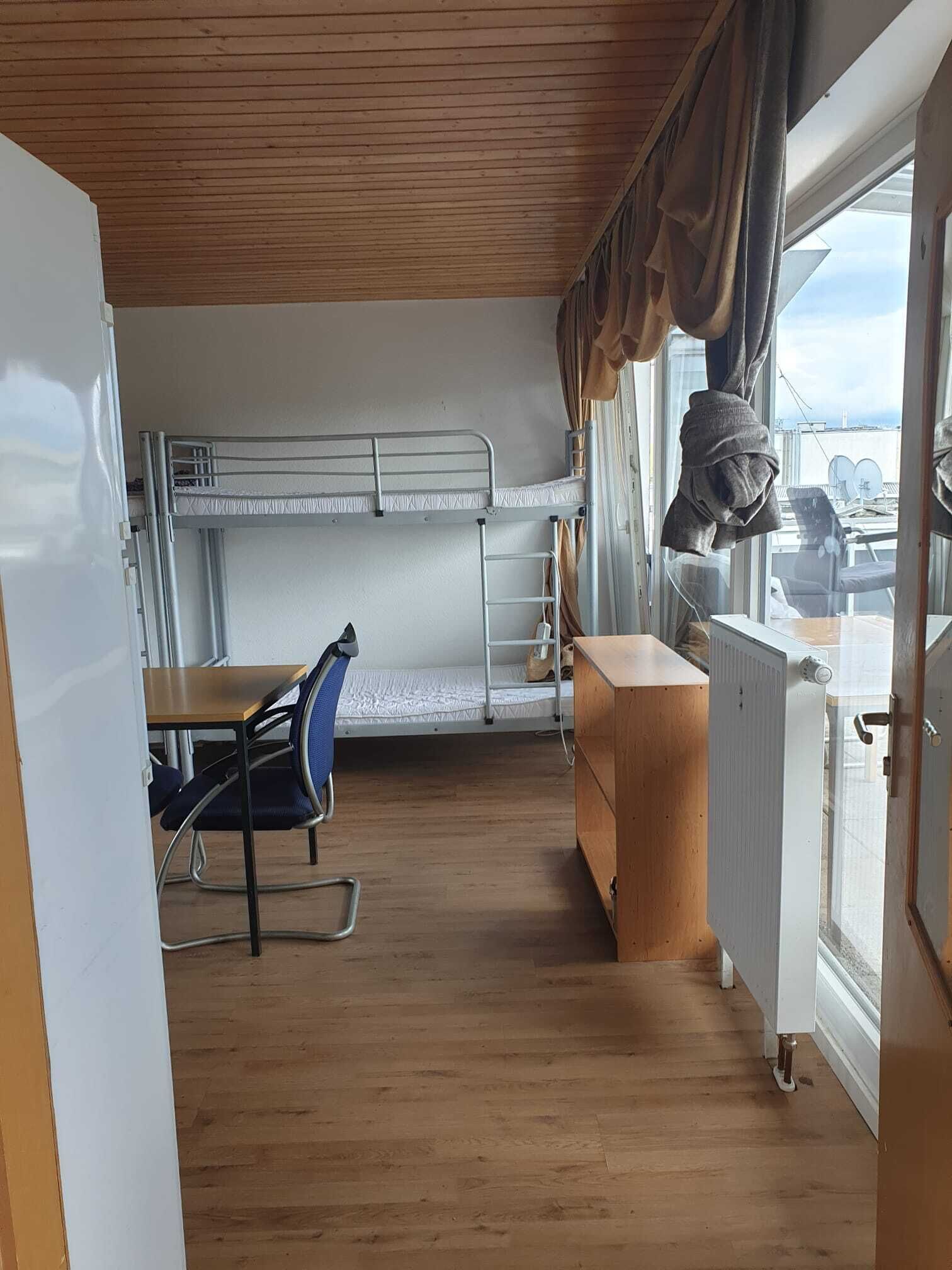 A compact cabin with bunk beds, a small table with a chair, and a window with curtains.