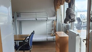 Uma cabana compacta com beliches, uma mesa pequena com uma cadeira e uma janela com cortinas.