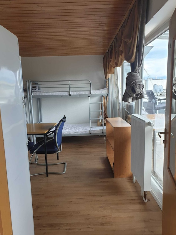 Uma cabana compacta com beliches, uma mesa pequena com uma cadeira e uma janela com cortinas.