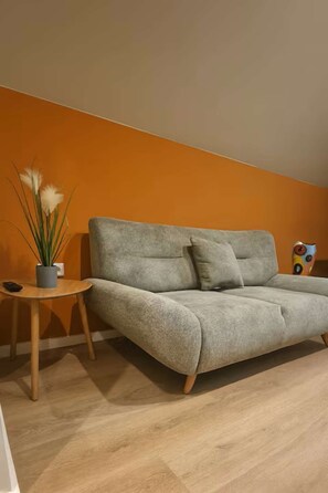 Un salon avec un canapé gris, une petite table d’appoint en bois et une plante en pot.