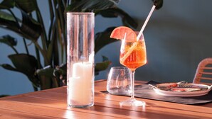A table with a tall glass of water, a glass with a drink and a slice of fruit, and a plate with food. - Locanda L'orangerie (Crespellano)