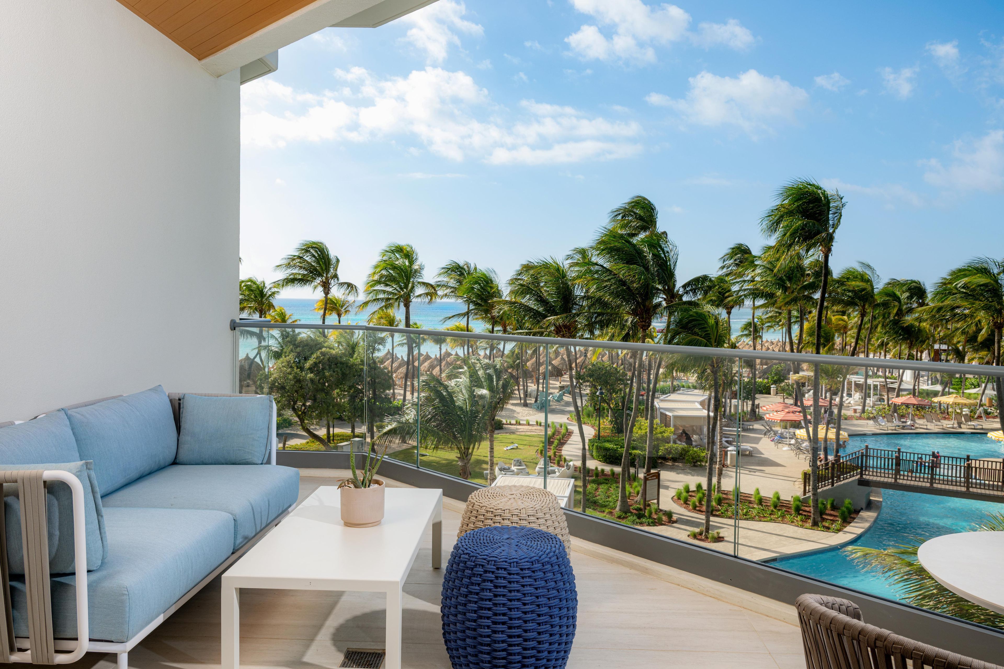 A balcony with a sofa, a table, and a view of a pool and palm trees.