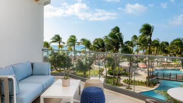A balcony with a sofa, a table, and a view of a pool and palm trees.