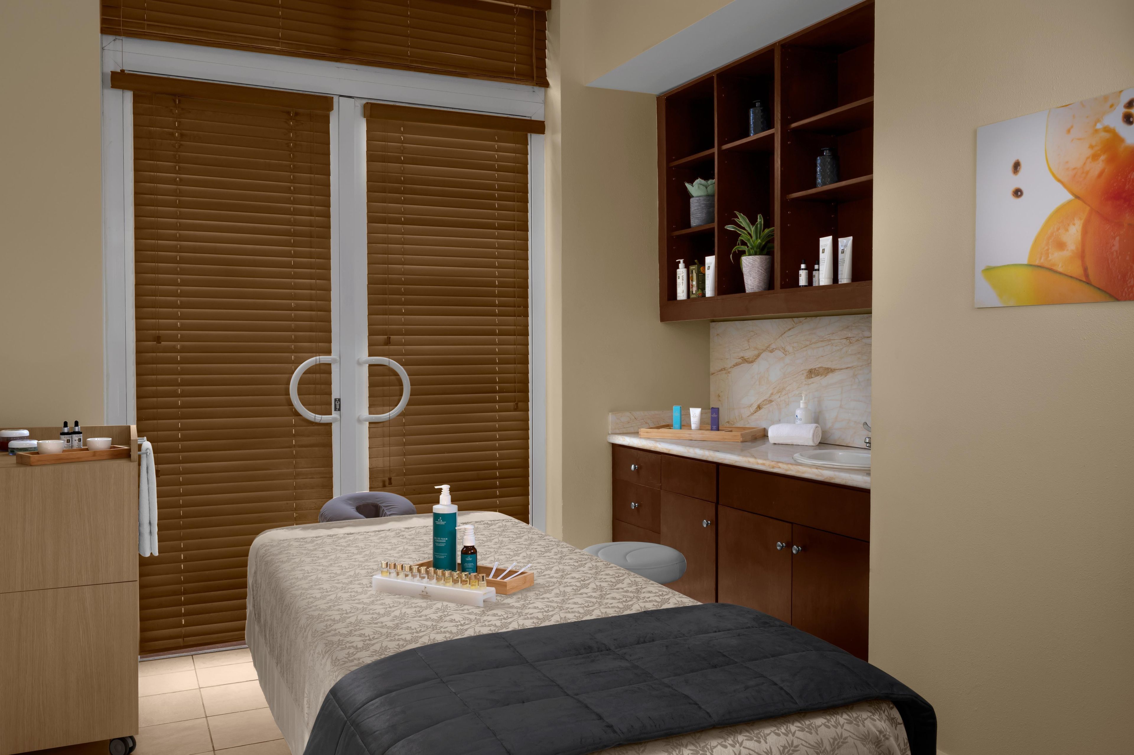 A room with a bed, a wooden cabinet with skincare products, a mirror, and a painting on the wall.