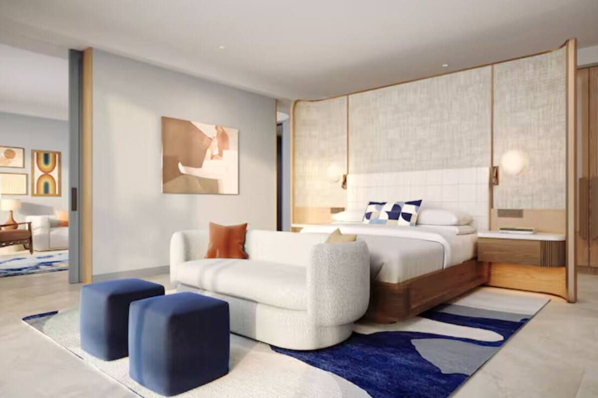 Ein modernes Schlafzimmer mit einem großen Bett, einer Couch und Poufs, einem großen Fenster und Blick auf die Stadt.