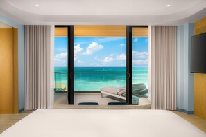 Une chambre avec un grand lit, une vue sur l’océan et un balcon équipé d’une chaise et d’une table.