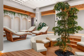 Un espace spa moderne avec des chaises longues en bois, un coin salon central et un grand arbre.
