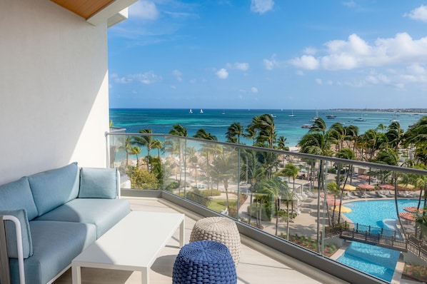 Un balcon avec vue sur l’océan, une piscine et un espace détente avec un canapé et un pouf.