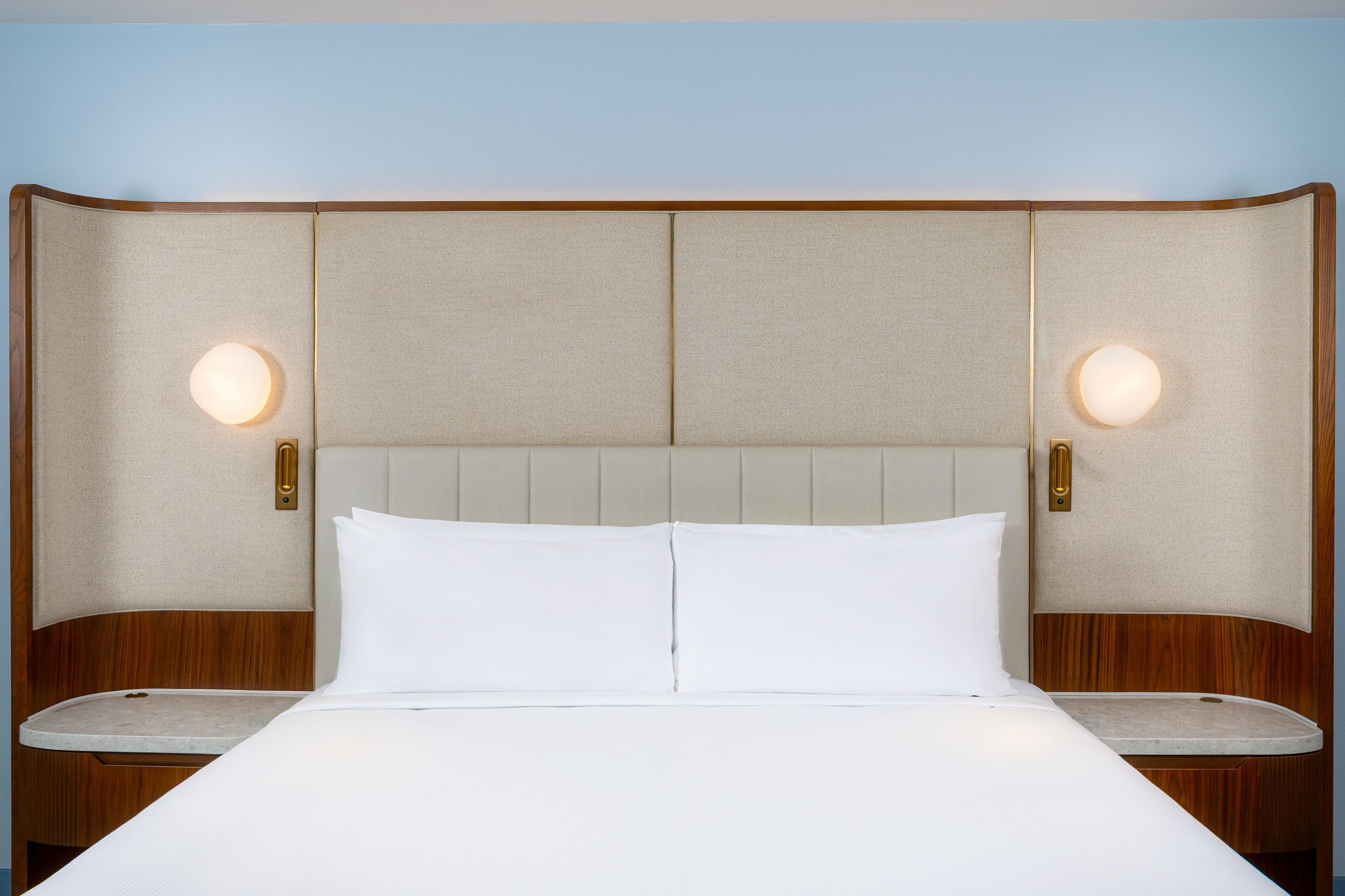 Habitación de hotel con una cama grande, dos mesitas de noche y un cabecero con luces empotradas.