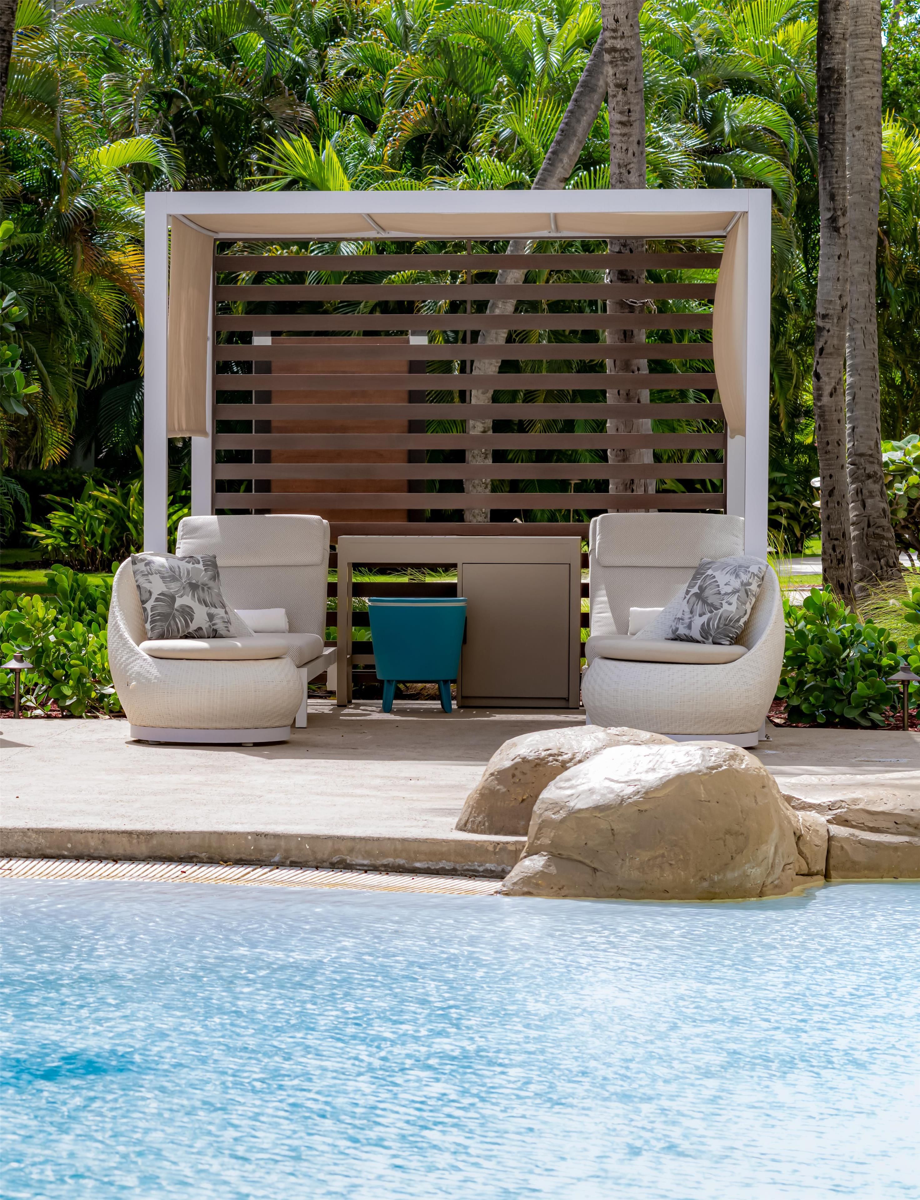 Ein Poolbereich mit zwei weißen Sitzliegen, einem kleinen blauen Tisch und einer Holz-Pergola.