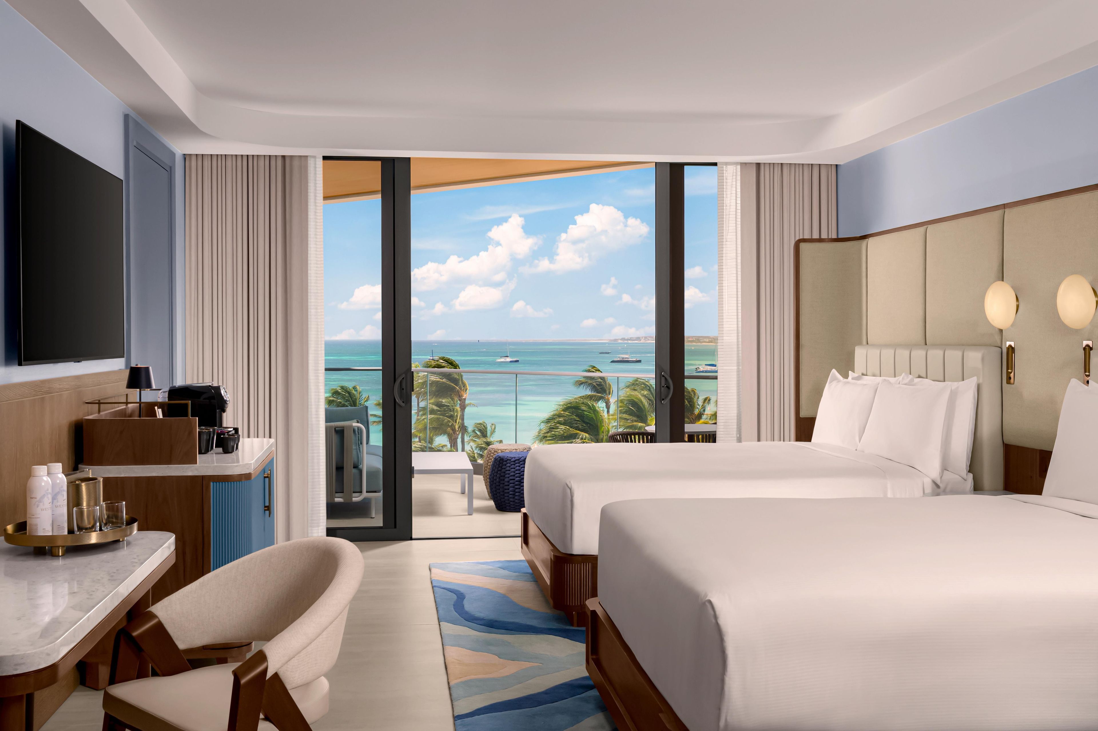 A hotel room with a balcony, a bed, a desk, a chair, and a TV.