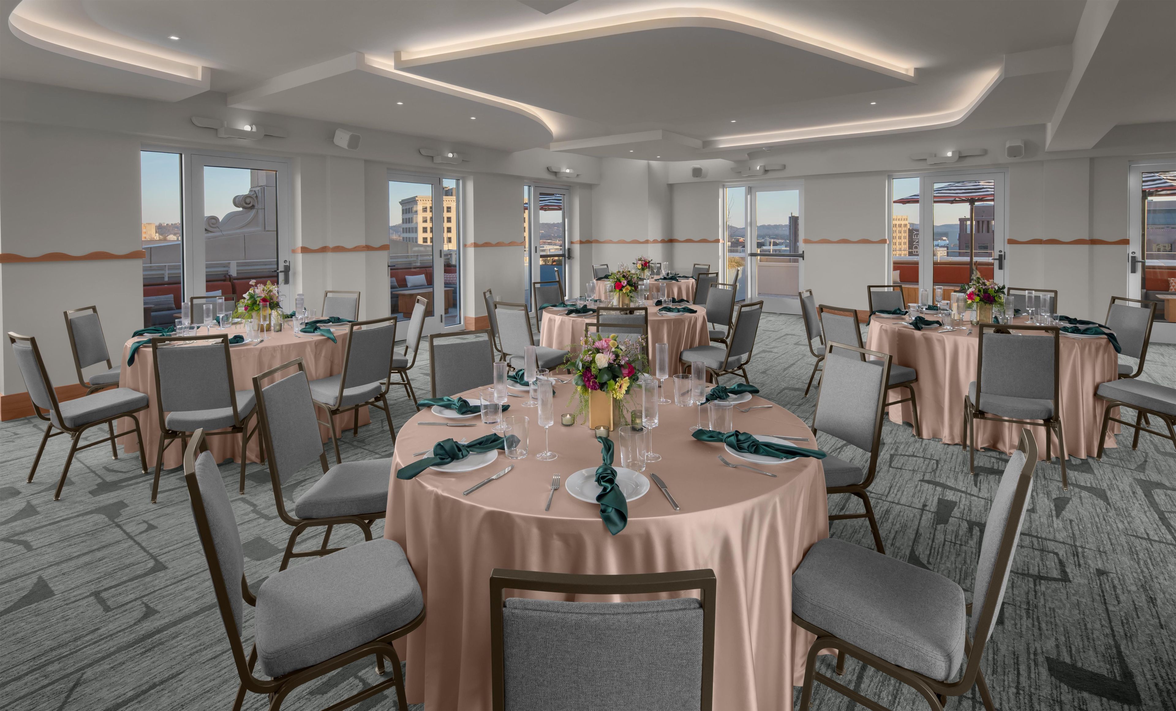 A conference room with round tables, chairs, and a view of the cityscape through large windows.