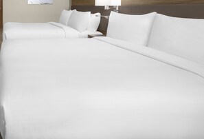 Una cama bien hecha con sábanas blancas, cabecera de madera y mesita de noche con una lámpara.