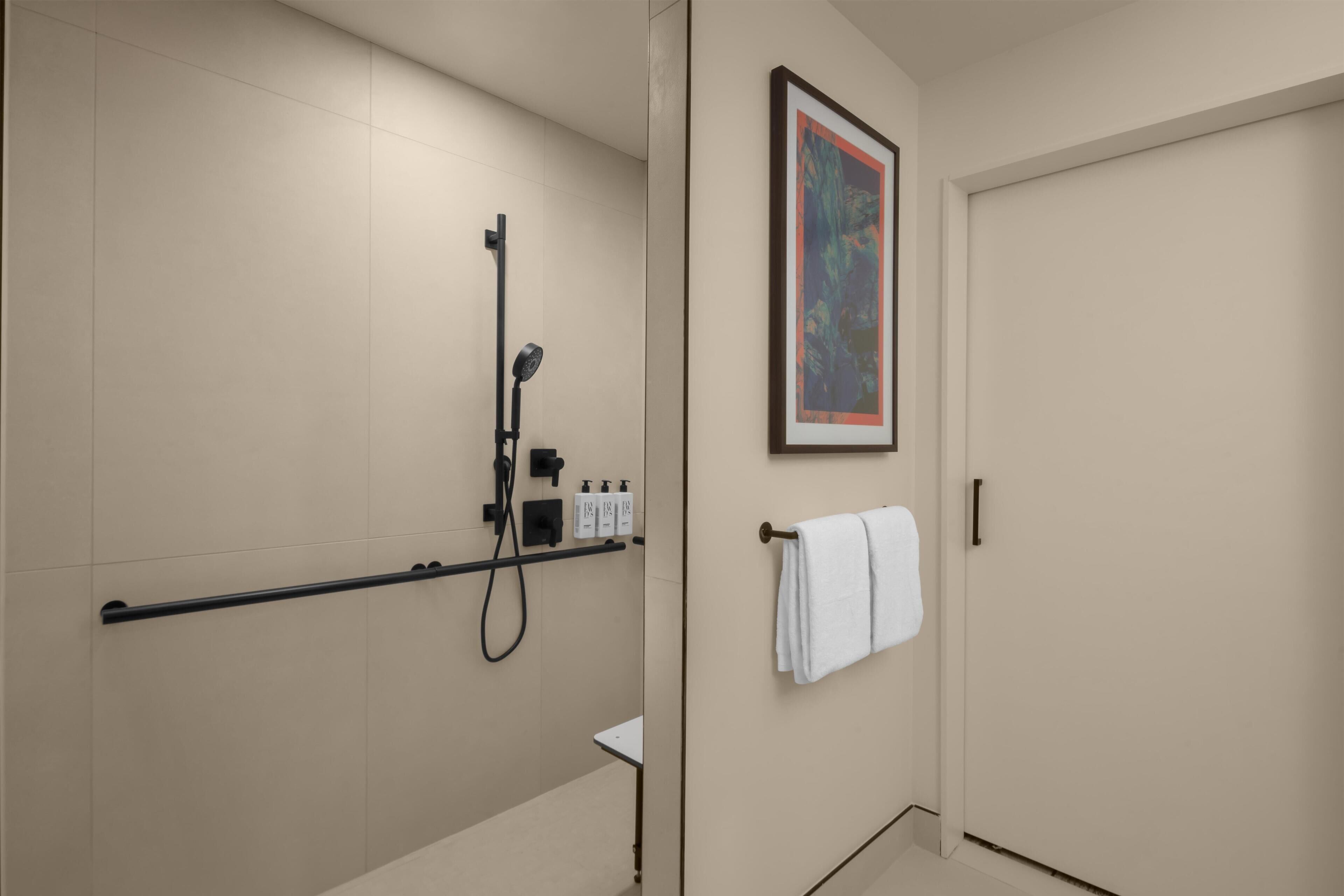 A modern bathroom with a shower, a towel rack, and a framed artwork on the wall.