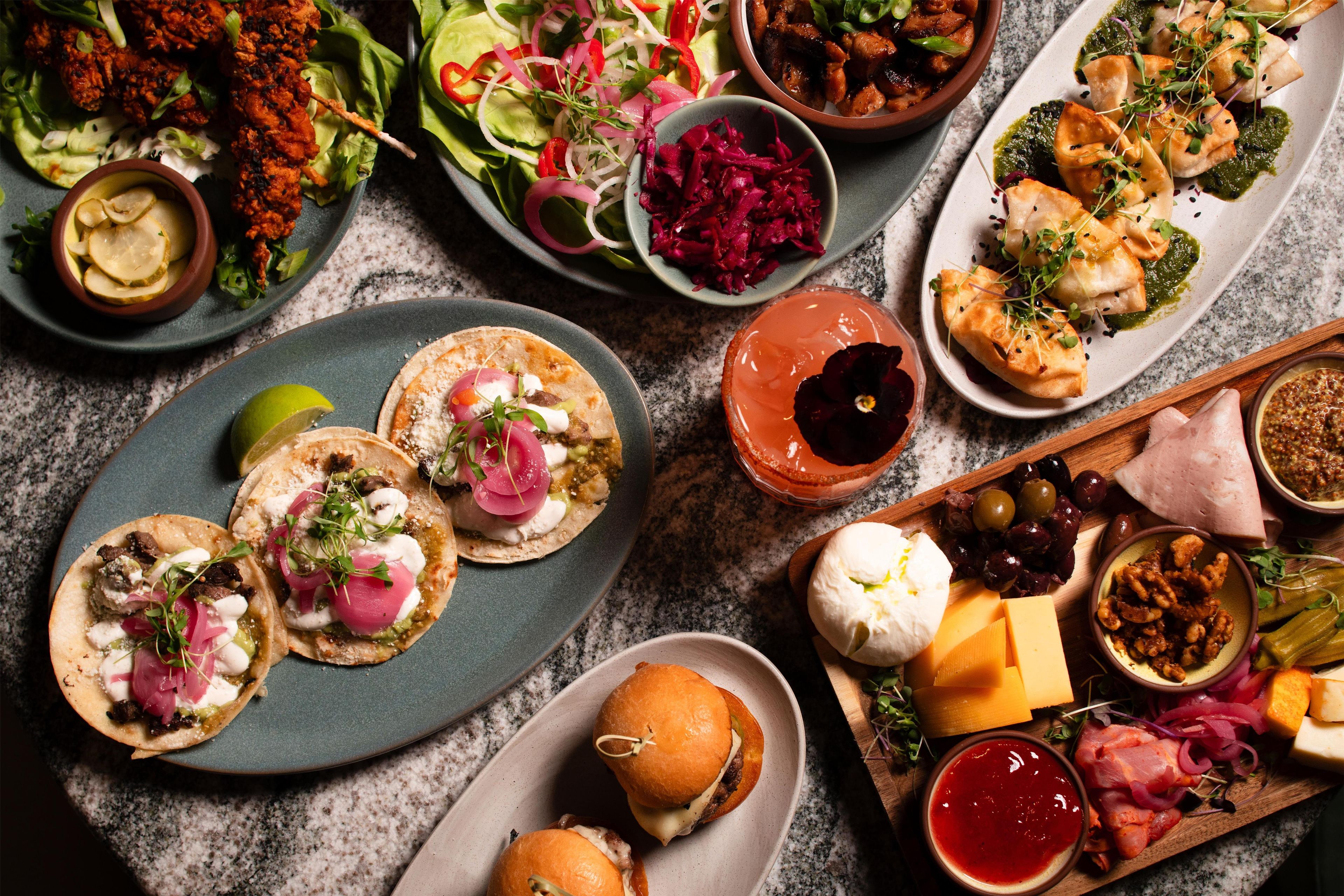 A variety of food items including tacos, a burger, and a selection of cheeses and olives.