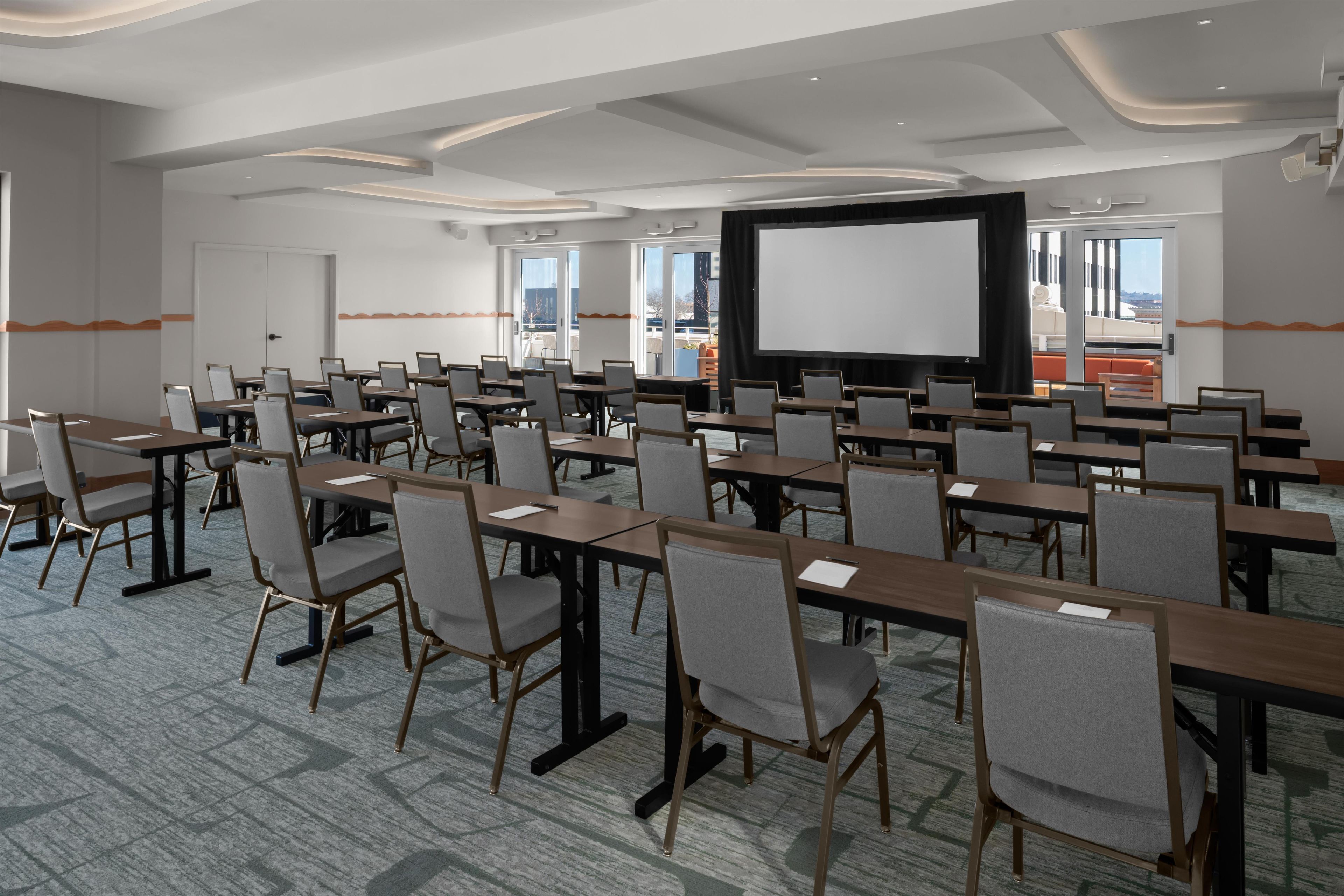 Une salle de conférence équipée de plusieurs tables et chaises, d’un grand écran et offrant une vue sur l’extérieur.