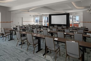 Un salón de conferencias con varias mesas y sillas, una pantalla grande y vistas al exterior.