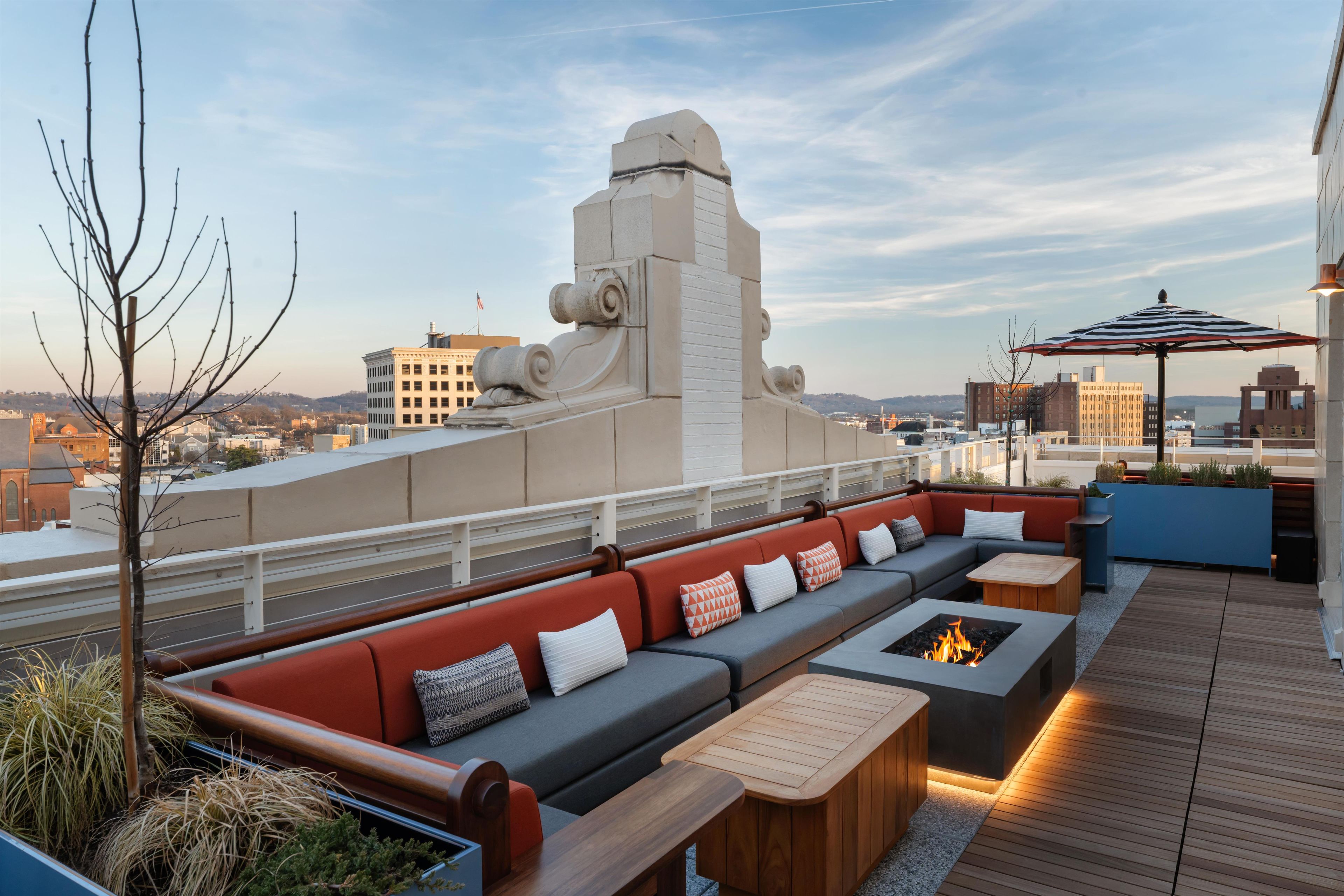A rooftop terrace with a long sofa, a fire pit, and a view of the cityscape.