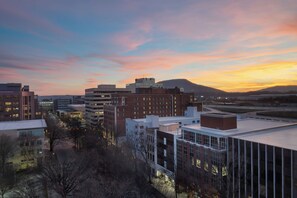 Un paisaje urbano al atardecer con edificios modernos, cielo despejado y colinas distantes.