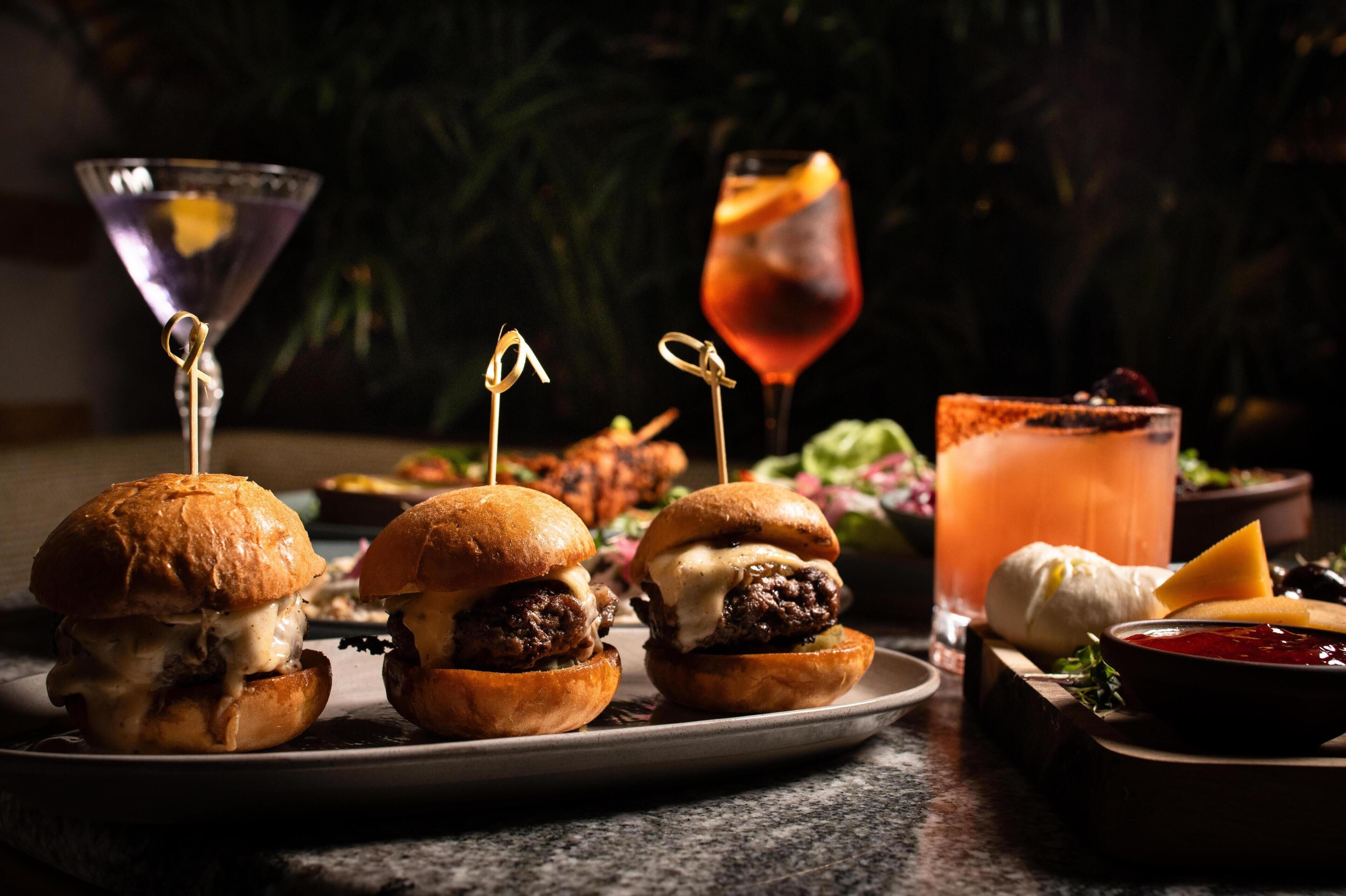 A plate with three burgers, a martini glass, and a cocktail with garnish.