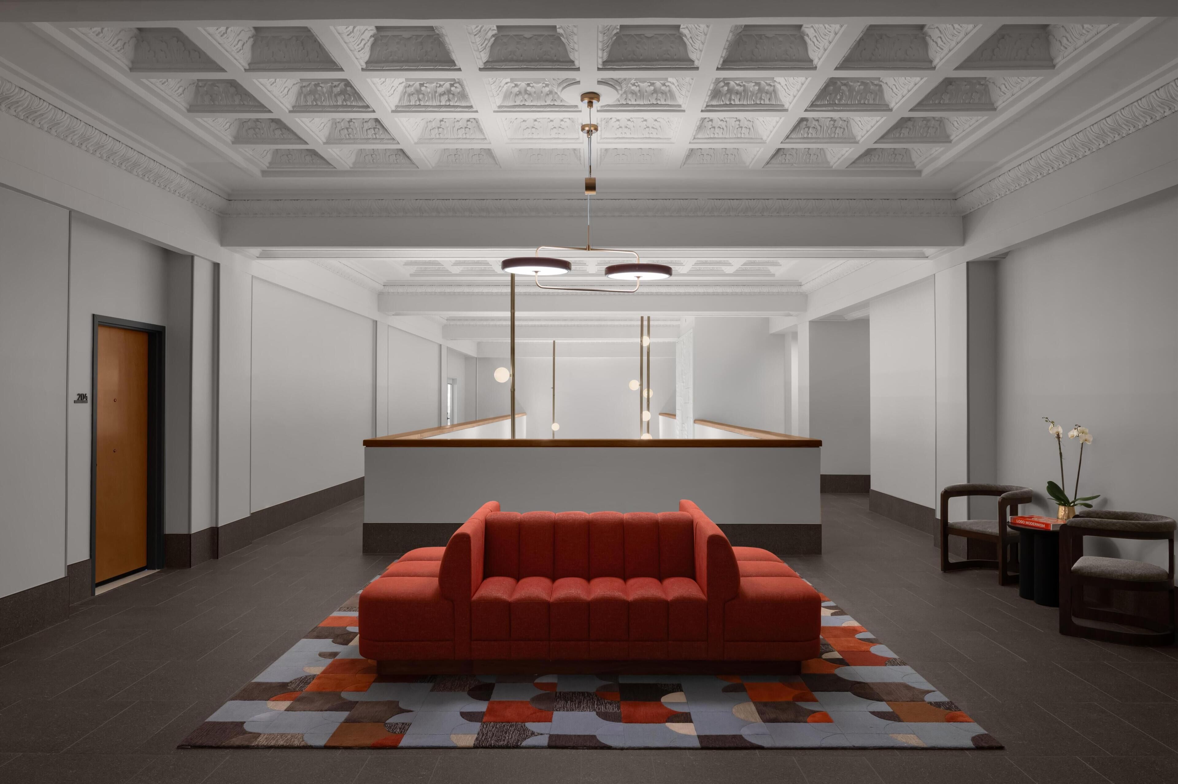 Eine großzügige Lobby mit einem roten Sofa, einem gemusterten Teppich und einer Decke mit aufwendigen Schnitzereien.