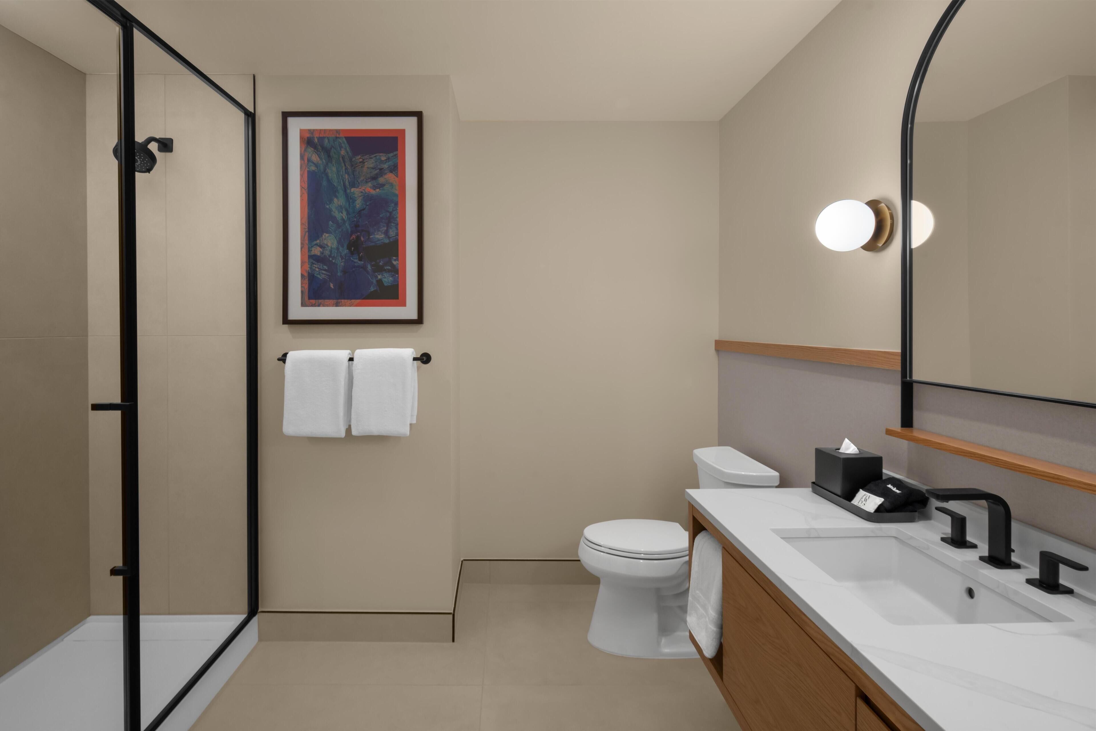 Ein modernes Badezimmer mit Duschkabine aus Glas, Toilette, Waschbecken mit Spiegel und einem gerahmten Kunstwerk an der Wand.