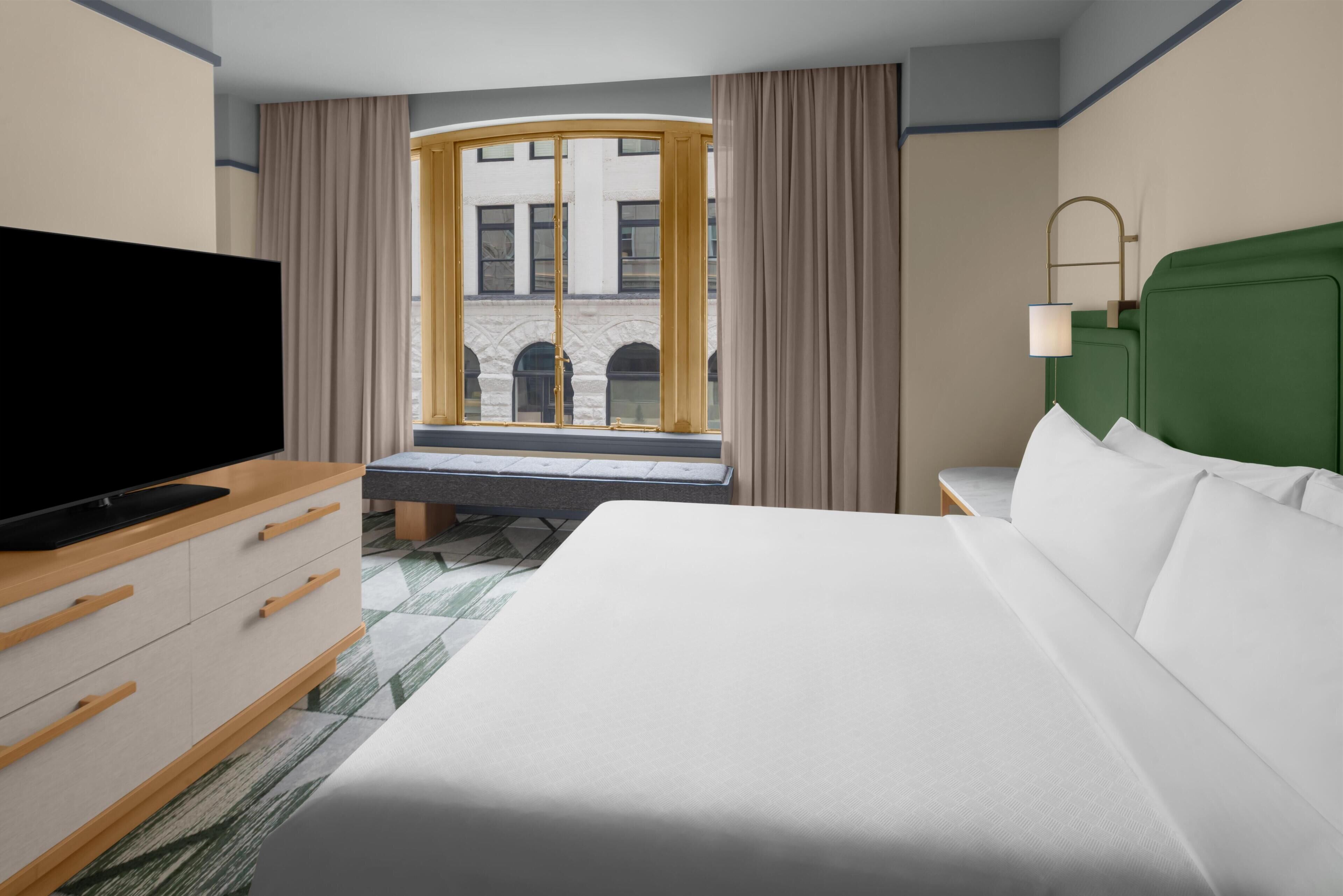 Une chambre d’hôtel avec un lit, une télévision, un bureau et une fenêtre avec des rideaux.