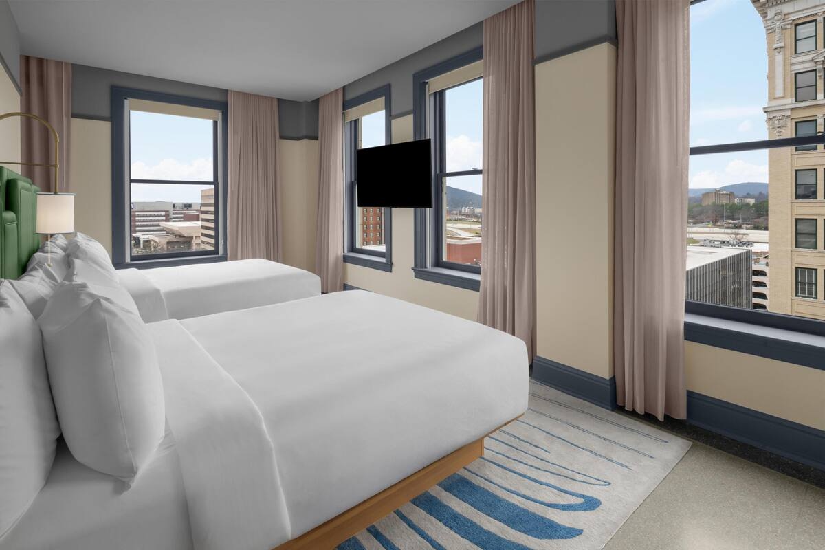 Une chambre d’hôtel avec un grand lit, deux fenêtres, un téléviseur à écran plat et une vue sur le paysage urbain.