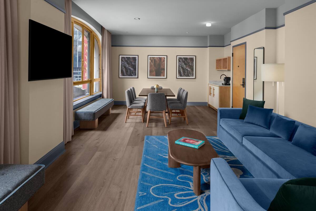 Une chambre d’hôtel moderne dotée d’un coin repas, d’un canapé, d’une télévision et d’œuvres d’art accrochées aux murs.